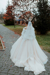 A woman in a white dress is walking down a path with leaves on the ground. She is wearing a white veil and a crown