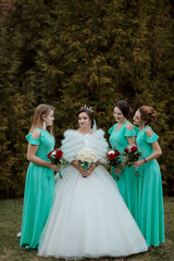 Fototapeta premium A bride and her bridesmaids pose for a picture. The bride is wearing a white dress and a green jacket