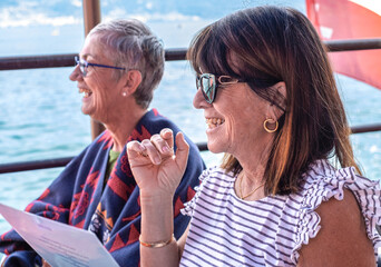 Portrait of two joyful senior women sitting at restaurant table at the Lake Geneva enjoying travel, tourism, freedom and good day. Relaxed retirement lifestyle