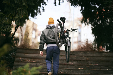 Naklejka premium Man Carrying Bicycle Up Steps in Urban Park