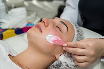woman is lying in beauty salon and receive nourishing moisturizing cream of her face
