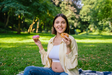 Dark-haired young pregnant woman holding donuts and looking anticipated
