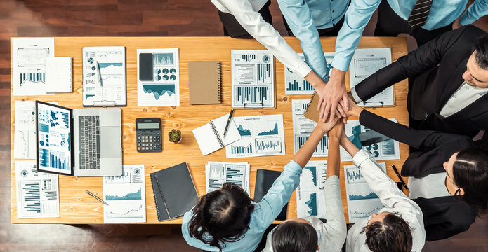 Panorama top view multiracial business people make synergy hand stack together over table with financial paper as analyst team building collaboration for corporate employee in workplace.Meticulous