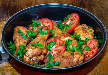 Fried chicken legs with tomatoes and parsley on a wooden surface