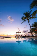 Fototapeta premium Infinity pool at a luxury tropical resort reflecting palm trees and a vibrant sunset sky, creating a peaceful and picturesque beach scene. Generative AI