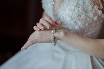 A woman is wearing a pearl bracelet and is touching her wrist. The bracelet is made of gold and has a diamond design. The woman is sitting on a chair and she is admiring her bracelet