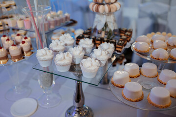 A table full of desserts including cupcakes, pastries, and cakes. The desserts are arranged on a glass table and are displayed in a way that makes them look appealing and inviting