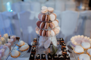 A dessert table with a tall stack of macarons on top. The table is filled with various desserts, including cakes, cookies, and pastries. The atmosphere is elegant and inviting