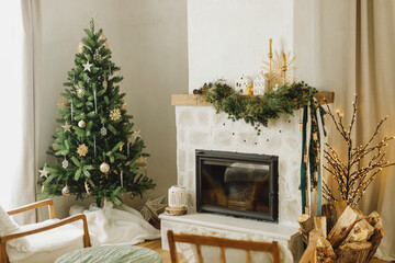 Stylish decorated christmas tree with vintage ornaments and modern decor of fireplace mantel with fir branch, bells, ribbon and garland light. Atmospheric xmas holidays at home. Merry Christmas!
