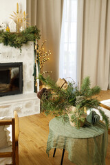 Stylish christmas decorated living room with christmas tree and modern fireplace mantel with fir branch, bells, ribbon and garland light. Atmospheric xmas holidays at home. Merry Christmas!