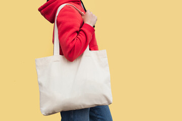Woman in red hoodie holding tote canvas blank eco bag on street light yellow minimal wall...