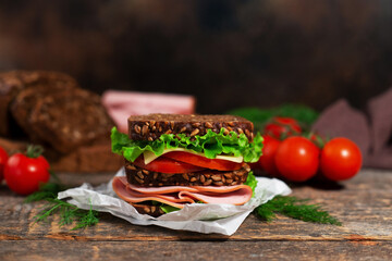 Sandwich with sliced ham, lettuce, tomato and cheese, served on a wooden board. Close-up.