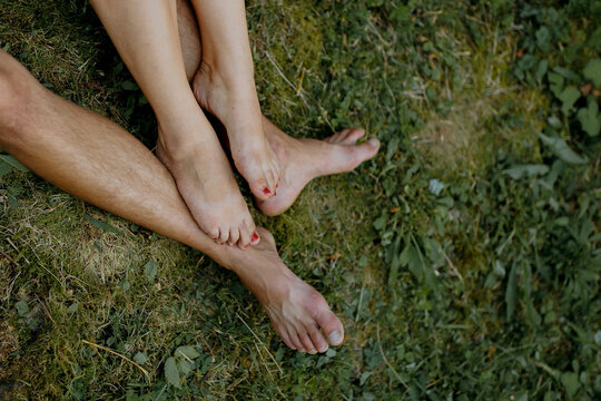 A couple is sitting on the grass with their feet touching. Scene is romantic and intimate - Powered by Adobe