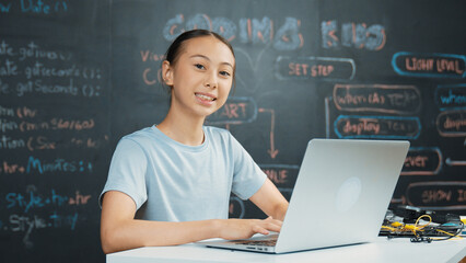 Smart girl programing system by using laptop at blackboard. Highschool student writing engineering code or prompt while looking at camera at STEM technology class. Creative education. Edification.