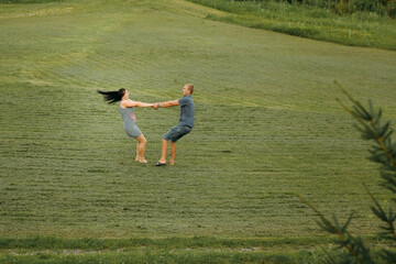 A couple is playing in a field, with the man holding the woman's hand. Scene is lighthearted and playful