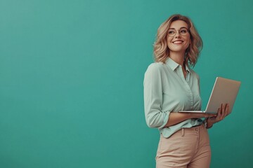 Joyful female entrepreneur in casual business attire, holding a laptop, smiling confidently. Portrait on solid teal background. Ideal for small business promotions, coaching services, financial.