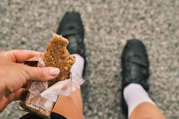 Close-up photo of a person's hand holding a granola bar with a bite taken out of it. The person is...