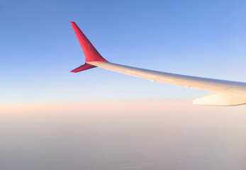 Fototapeta premium Wing from airplane window on cloudy day. Aerial view of clouds through a plane window. Wing of airplane with foggy clouds