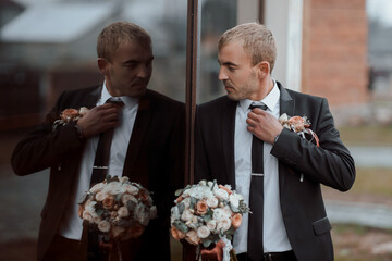 A man in a suit is getting ready for a wedding. He is wearing a tie and a boutonniere