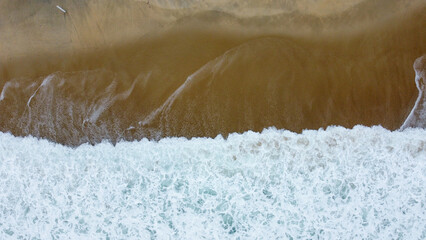 Foto aérea de ondas quebrando na praia, capturando a beleza do mar e o movimento das ondas com a areia ao fundo