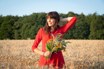 Hübsche Frau  mit einem Blumenstrauß in der Hand steht glücklich in einem reifen Getreidefeld.