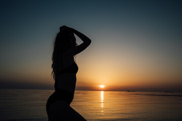 Silhouette of slender woman in sea water at sunset