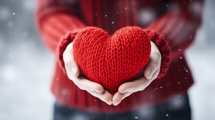 Fototapeta premium Embracing love hands cradling a knitted red heart against a snowy backdrop of friendship