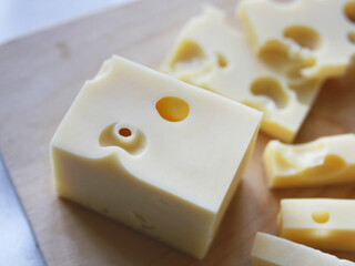 A block of cheese with large holes on a wooden board on a white background. Maasdam cheese and radomer. Cheese making and production of milk products. Healthy nutrition