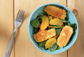 Salad with grilled halloumi cheese, orange and carrots in a blue bowl