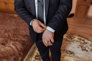 A man in a suit is getting ready for a formal event. He is adjusting his tie and putting on a ring. Concept of formality and preparation for a special occasion
