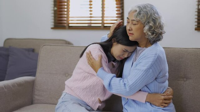 Grandmother comforting her sad granddaughter on a sofa in their living room, sharing love and emotional support