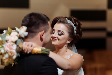 A bride and groom are embracing each other with a bouquet of flowers in the bride's hand