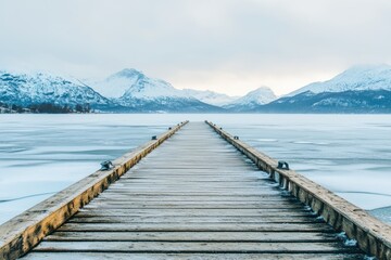 A wooden pier with a bridge leading to a body of water. The water is frozen and the sky is cloudy