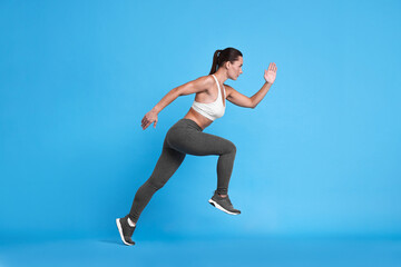 Obraz premium Woman in sportswear running on light blue background