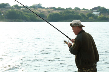 Fisherman with rod fishing near lake at summer