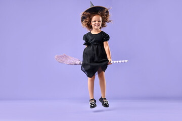 Funny girl with broom dressed like witch for Halloween celebration on violet background