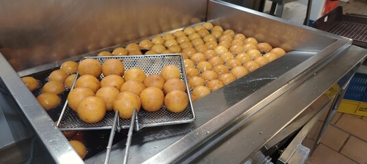 Golden, round buñuelos frying in hot oil, highlighting their crispy texture and irresistible aroma. A classic treat, especially popular during Christmas, perfect for enjoying with coffee or as dessert