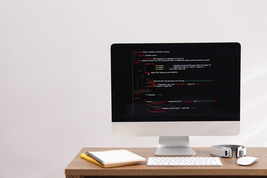 Programmer's workplace. Modern compter with unfinished code, headphones and stationery on desk indoors