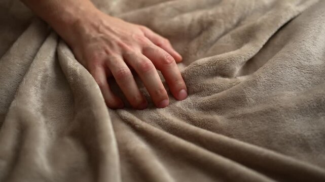 A man's hand touches a blanket.
The hand squeezes a warm blanket.
Brown blanket close-up.
Hand on the bed.
Man squeezing fabric