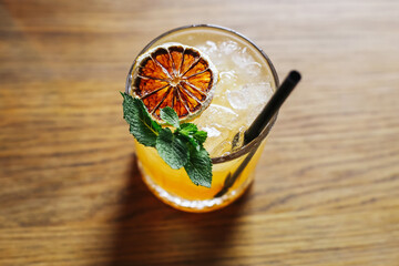 Whiskey sour cocktail in a glass on a wooden surface, garnished with an orange slice, fresh mint,...