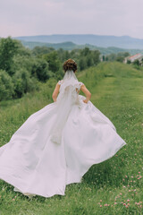 A woman in a white dress is walking through a field. The dress is long and flowing, and she is wearing a veil. The scene is peaceful and serene, with the woman's dress billowing in the wind