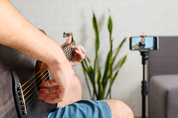 Online guitar lesson. Close-up of guitarist's hand against phone background. Selective focus on musician's fingers