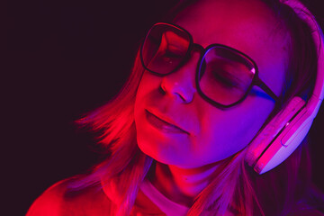 The woman closes her eyes, lost in the rhythm of music while wearing oversized headphones,...