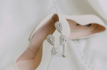 A pair of earrings are on a white shoe. The earrings are made of gold and diamonds