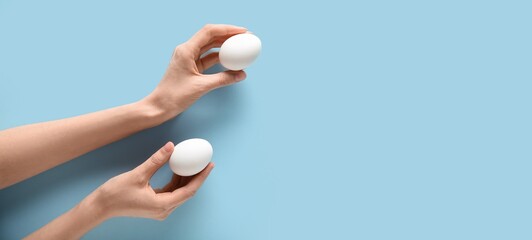 Hands holding raw chicken eggs on light blue background with space for text