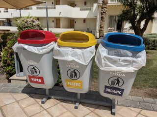 Three colorful trash bins for separate waste collection stand in a row outdoors under the sun.