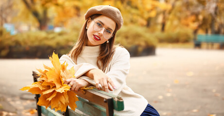 Stylish young woman sitting on bench in autumn park
