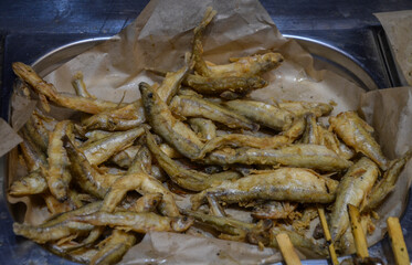 Appetizing golden-brown, deep-fried anchovies small fish arranged on a piece of brown paper. popular method of preparing seafood as an appetizer or snack at street food market