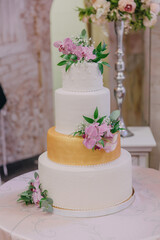A white and gold wedding cake with pink flowers on top. The cake is decorated with a gold trim and has a floral design