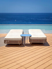Two sun lounger on a patio infront of a swimming pool against blue water of Atlantic Ocean and blue sky